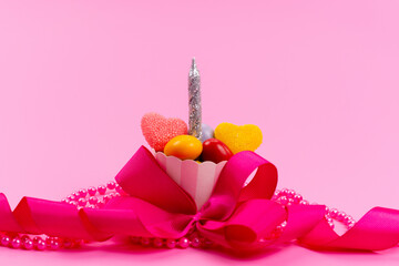 a front view little present with candies and silver candle designed with pink bow isolated on the pink desk present birthday celebration