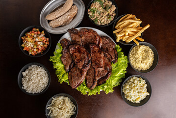 Churrasco - grilled sirloin steak with garnishes - rice, farofa, vinaigrette, potato salad, and fries