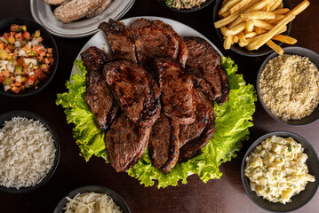 Churrasco - grilled sirloin steak with garnishes - rice, farofa, vinaigrette, potato salad, and fries