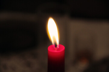 Gentle light from a burning red candle on a blurred background