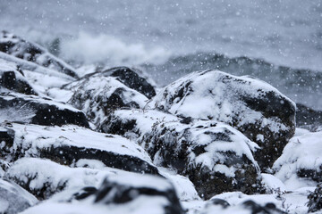 rocky costal black rock beach covered in falling snow, during winter storm