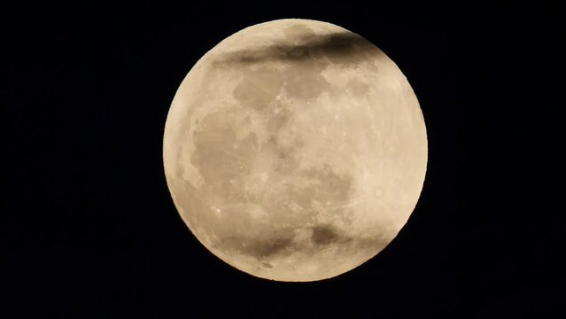 4k time lapse footage of clouds moving over bright full moon on dark black sky background, super telephoto lens effect.