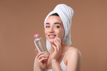 Beautiful woman in terry towel removing makeup with cotton pad on beige background