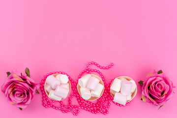 a top view white marshmallows inside paper packages along with pink roses on the pink desk sugar sweet confectionery