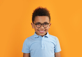 Cute African-American boy with glasses on orange background