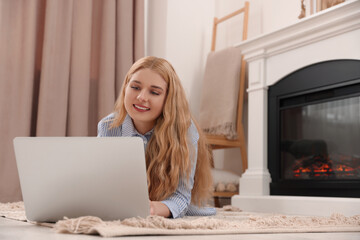 Fototapeta na wymiar Young woman working on laptop near fireplace in room