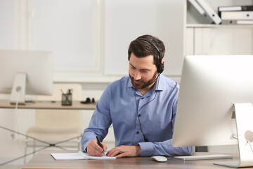 Fototapeta premium Hotline operator with headset working in office, space for text