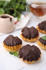 Delicious profiteroles with chocolate spread and mint on table, closeup