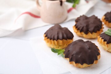 Delicious profiteroles with chocolate spread and mint on white table, closeup. Space for text