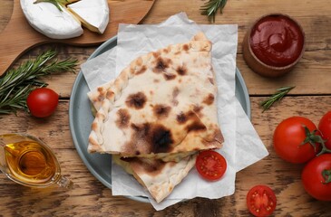 Tasty pizza calzones with cheese and different products on wooden table, flat lay