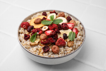 Oatmeal with freeze dried fruits, nuts and mint on white tiled table, closeup