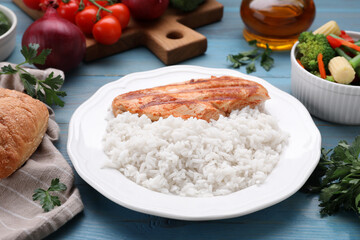 Grilled chicken breast and rice served with vegetables on light blue wooden table