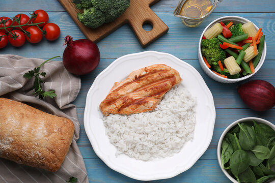 Grilled chicken breast and rice served with vegetables on light blue wooden table, flat lay
