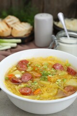 Delicious sauerkraut soup with smoked sausages and green onion on light grey table, closeup