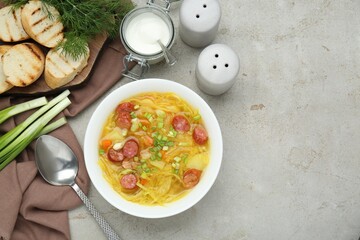 Delicious sauerkraut soup with smoked sausages and green onion served on light grey table, flat lay. Space for text