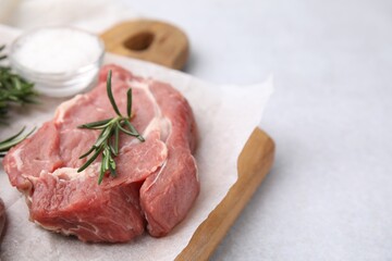 Fresh raw meat with rosemary on light table, closeup. Space for text
