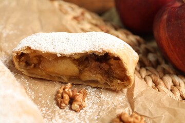 Piece of delicious apple strudel with walnuts and powdered sugar on parchment paper, closeup