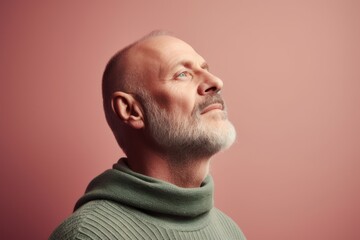 Portrait of a senior man in a green sweater on a pink background