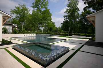 THE WOODLANDS, TEXAS - MAY 5th 2023: an outdoor pool and spa with water features on a hot sunny day. The blue water is sparkling and the Mediterranean style house is white with a terracotta roof.