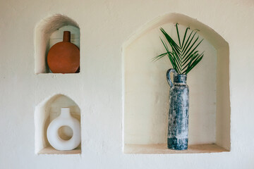 Frontal view of a mediterranean interior A white wall with three niches in which beautiful vases...