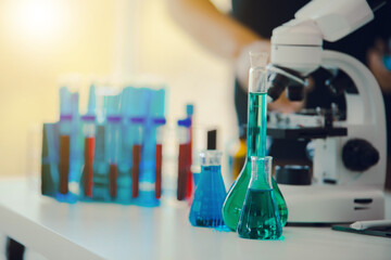 medical or scientific researcher researching and experimenting Multi-colored solution, vial and microscope In the laboratory or in the laboratory by wearing blue gloves and white clothing completely.
