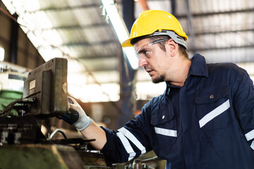 Professional caucasian white ethnicity male technician operating the heavy duty machine in the lathing factory. Technician in safety and helmet suit controlling a machine in factory.