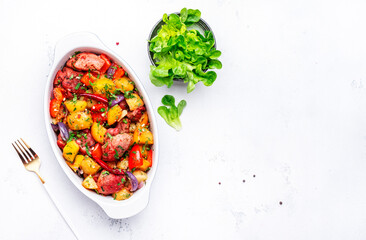Baked spicy turkey ragout with potatoes, paprika, red onion, herbs and spices in oval ceramic baking dish, white table background, top view, copy space