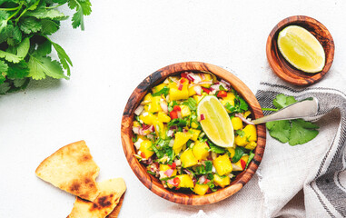 Mango salsa - spicy sauce with chili peppers, onion, garlic, lime and cilantro in wooden bowl on white table background, top view