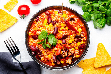 Chili con carne with minced beef, red beans, paprika, sweet corn and hot peppers in spicy tomato sauce, tex-mex cuisine dish, white table background, top view