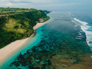 Tropical beach with cliffs, ocean and sunshine in Bali island. Aerial view of vacation beach