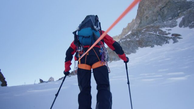 A mountaineer hikes up a snowy mountain with his crampons, harness and rope, in Alps, France 	