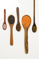 White background - Himalayan pink salt, poppy seeds, chia seeds, pink lentils and oregano on wooden spoons