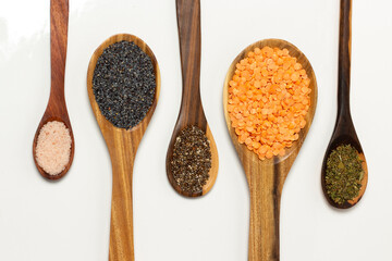 Himalayan pink salt, poppy seeds, chia seeds, pink lentils and oregano on wooden spoons - White background