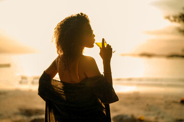 African woman drinking cocktail juice when stranding at tropical beach. Young traveler wearing...