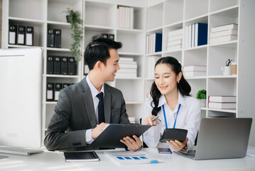 Asian business colleague business presents and explains and using laptop and tablet. Teamwork, financial marketing team, while sitting in office room.