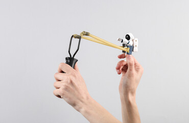 Hands holding slingshot with toy astronaut on gray background.