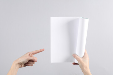 Female hands hold a blank magazine mockup with white pages on gray background