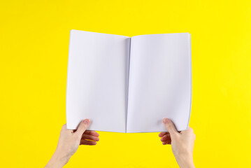 Female hands hold a blank magazine mockup with white pages on yellow background