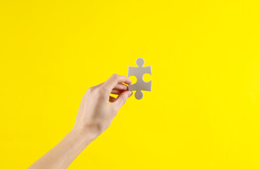 Woman's hand holds a jigsaw puzzle on yellow background. Business concept
