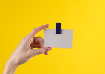 Hand holds a badge on a clip, yellow background