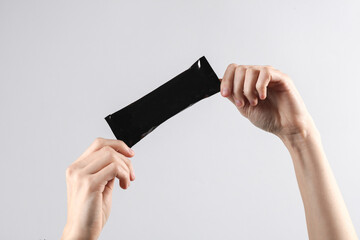 Hands holding a black pack of a bar or protein on gray background