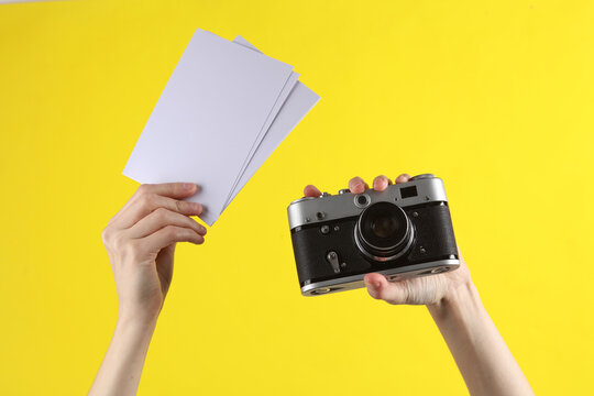 Female hands holds a camera and blank photographs on yellow background. Photographer, traveler. Template for design