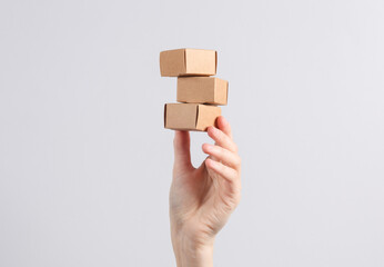 Hand holds a stack of craft boxes, miniature parcels on a gray background