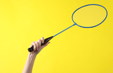 Hand holding batbinton racket on yellow background