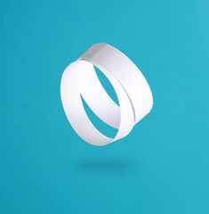 Two white paper bracelets levitating on a blue background with a shadow
