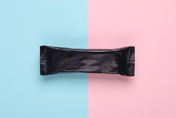 Black packaging of a chocolate or protein bar on a blue-pink pastel background