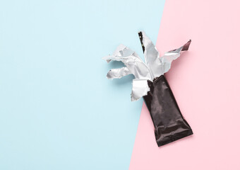 Empty open Black packaging of a chocolate or protein bar on pink blue background