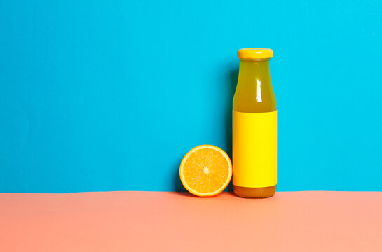 Bottle of orange juice with half juicy orange on blue pink background. Creative food layout