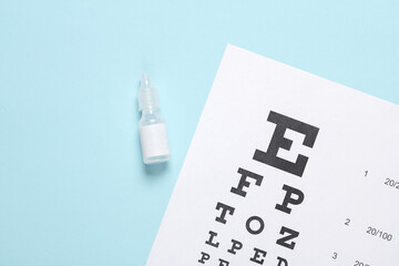 Eye test chart and eye drops bottle on blue background. Vision examination, correction
