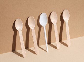 Plastic and wooden spoons on a beige background with shadow. Eco concept, plastic free, food....